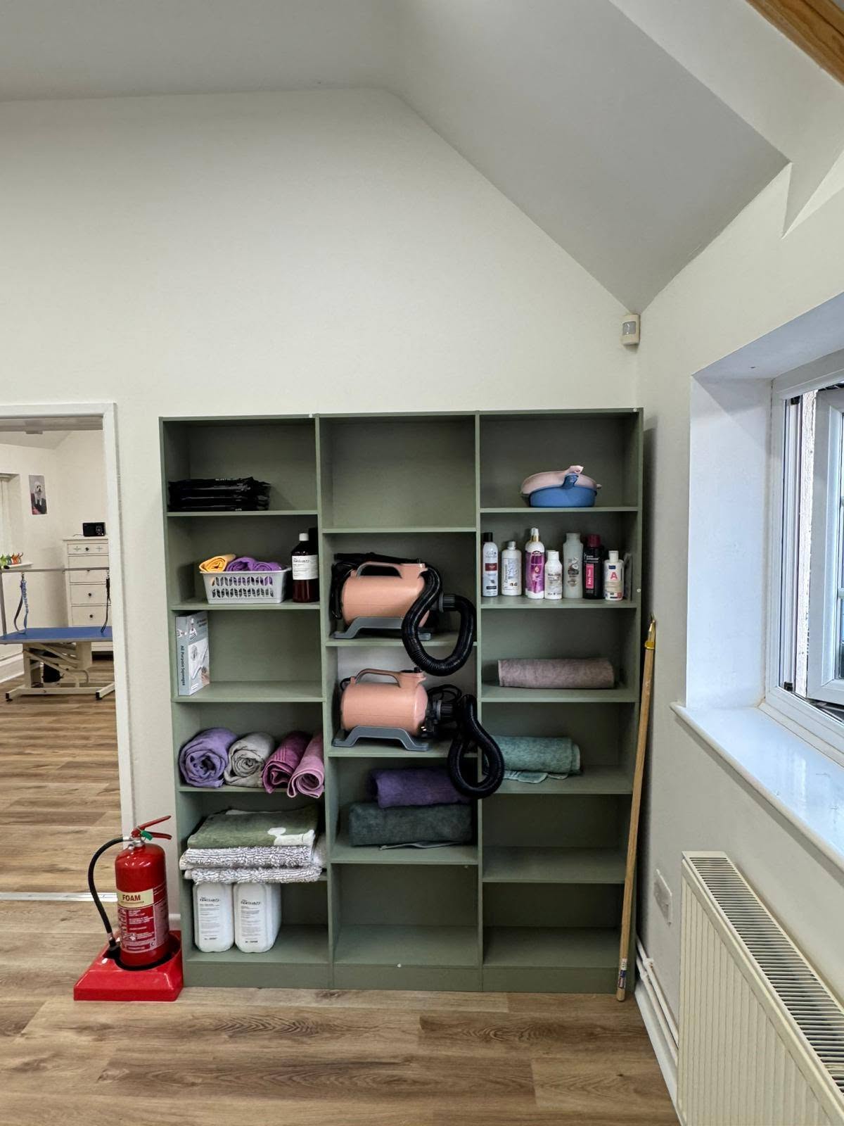 Sage-green shelving stacked with rolled towels, dryers and shampoos